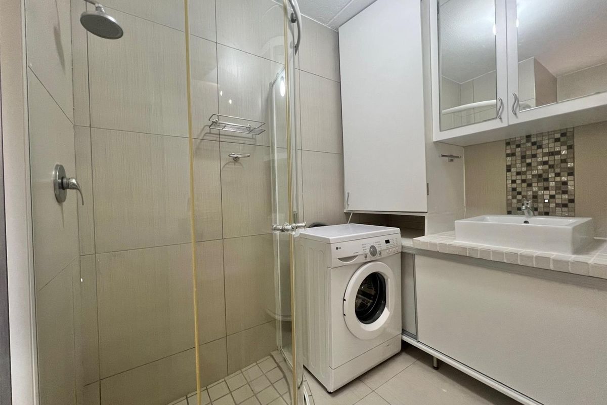 Compact bathroom featuring a glass-enclosed shower, built-in vanity with vessel sink, mirrored medicine cabinet, and integrated laundry space.