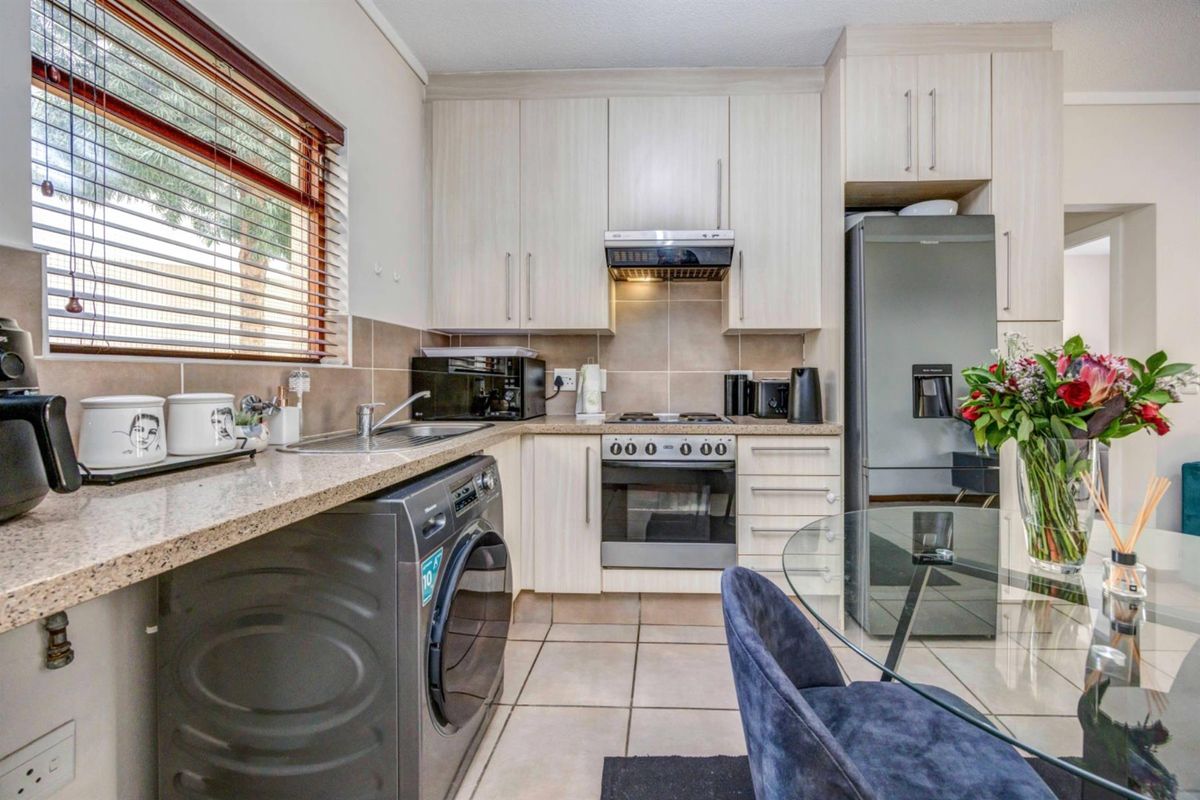 Compact kitchen featuring light-toned cabinetry, tiled backsplash, built-in oven with extractor fan, and integrated laundry plumbing.