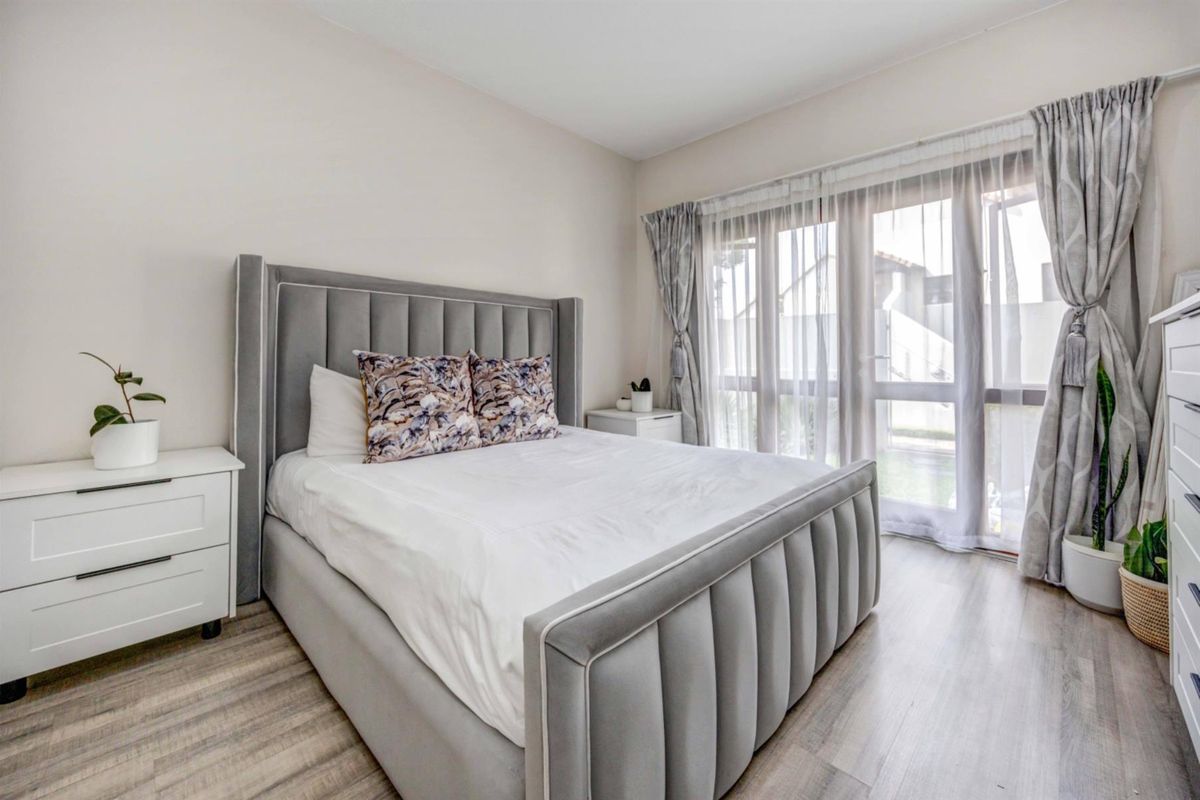 A bright and well-maintained bedroom featuring modern wood-look flooring and large glass sliding doors that provide ample natural light.