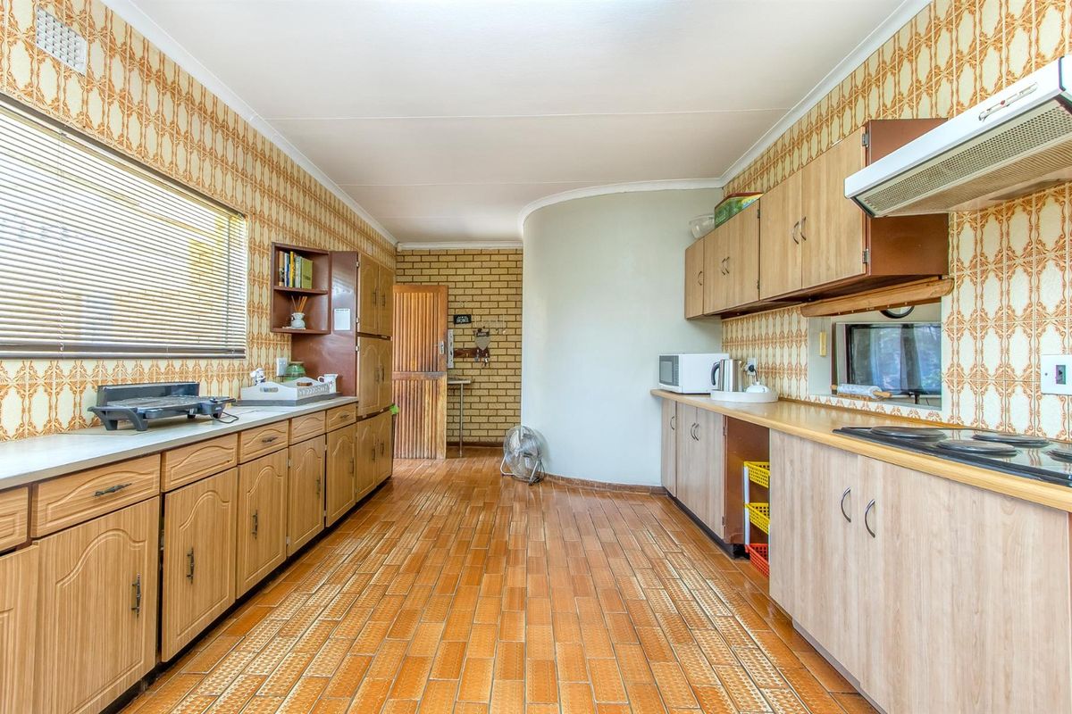 A dated kitchen featuring wood-look cabinetry, tiled flooring, and patterned wallpaper, offering a functional layout with built-in stove and extractor fan.
