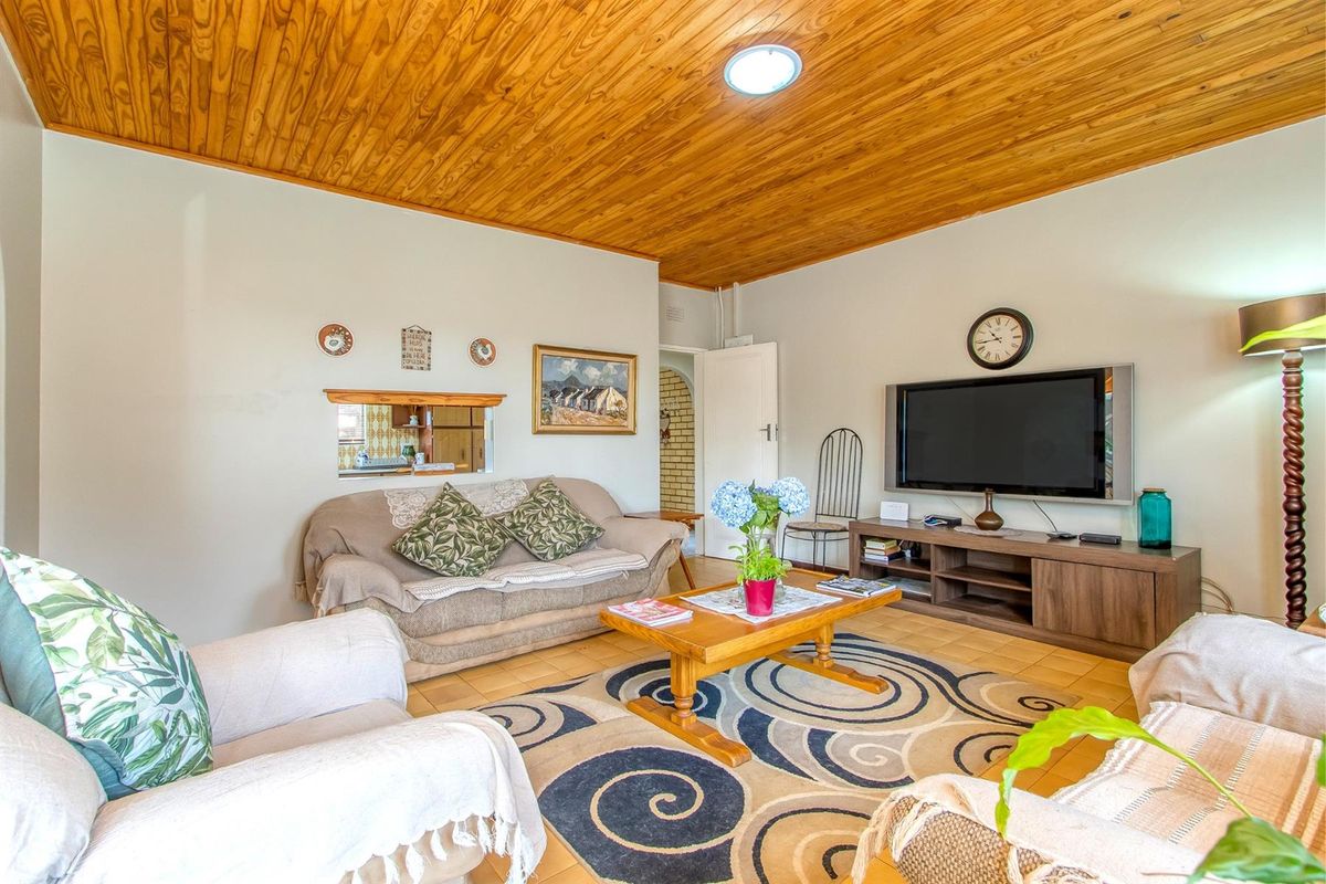 A comfortable living room featuring a warm wooden tongue-and-groove ceiling and tiled flooring, with a convenient serving hatch connecting to the kitchen area.