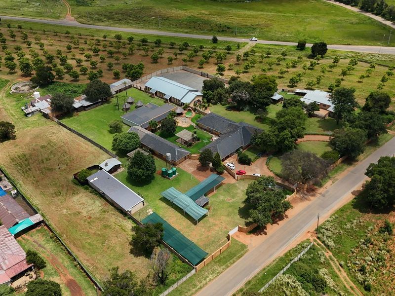 Aerial view of a small holding property featuring multiple outbuildings, extensive grounds, mature trees, and established access roads.