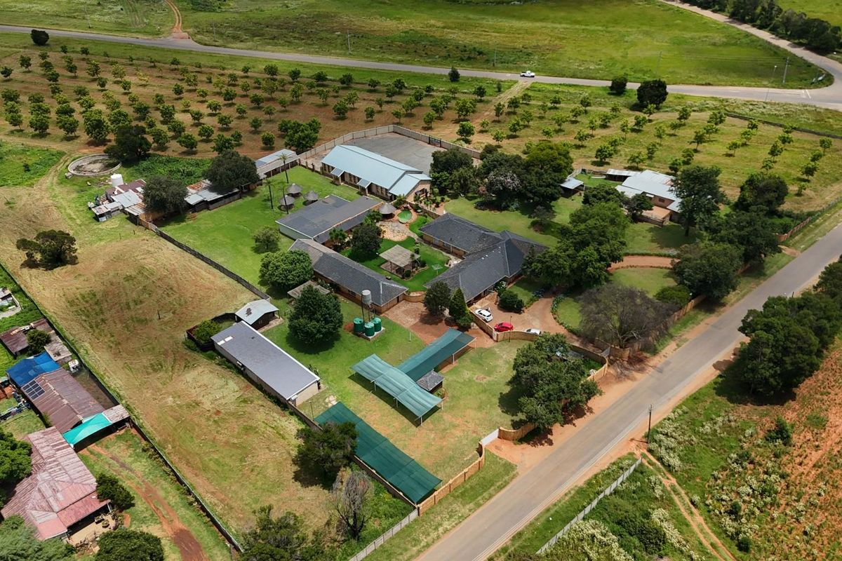 Aerial view of a small holding property featuring multiple outbuildings, extensive grounds, mature trees, and established access roads.