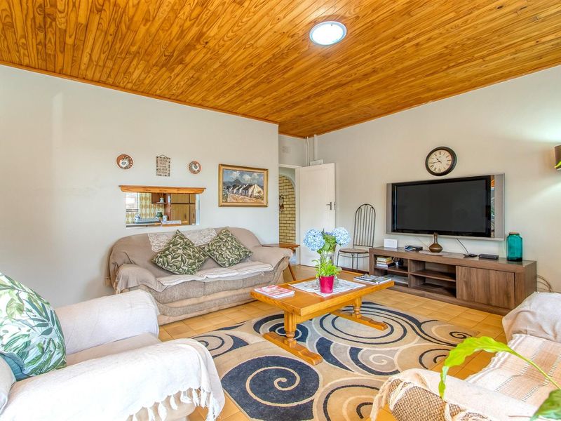 A comfortable living room featuring a warm wooden tongue-and-groove ceiling and tiled flooring, with a convenient serving hatch connecting to the kitchen area.