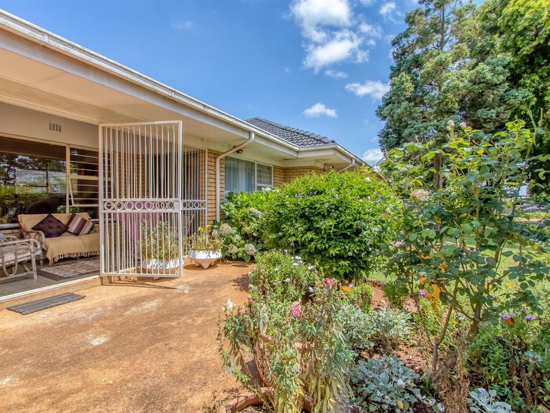 A view of the rear patio area featuring a concrete floor, security gate, and access to the interior, set against a landscaped garden.