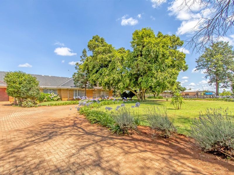 A spacious front exterior view of the small holding, featuring a paved driveway, established garden, and mature trees leading to the main residence.