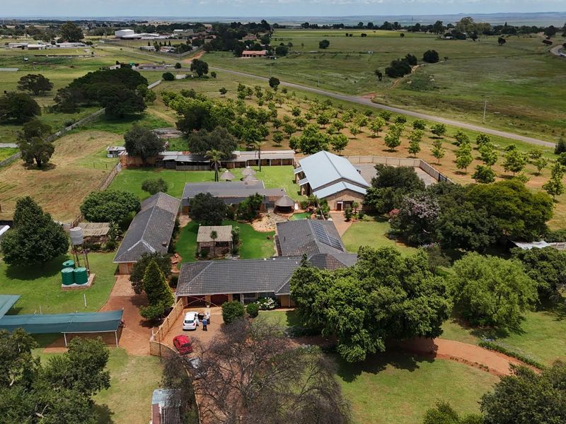 Aerial view of a spacious small holding featuring multiple residential buildings, outbuildings, expansive lawns, mature trees, and a large agricultural or storage shed.