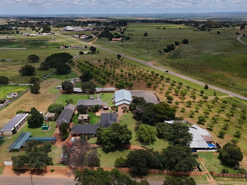 Aerial view of a small holding property featuring multiple outbuildings, extensive garden areas, mature trees, and surrounding agricultural land.