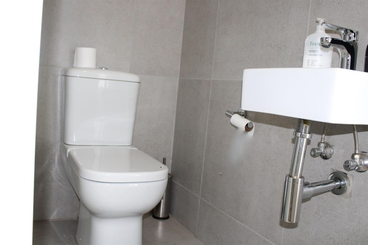 A compact guest bathroom featuring modern grey wall tiles, a white ceramic toilet, and a wall-mounted basin with chrome plumbing fixtures.