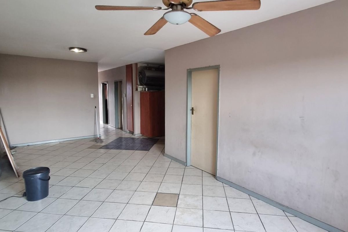 An empty living area featuring tiled flooring, a ceiling fan, and neutral wall tones, offering a blank canvas for renovation or interior design updates.
