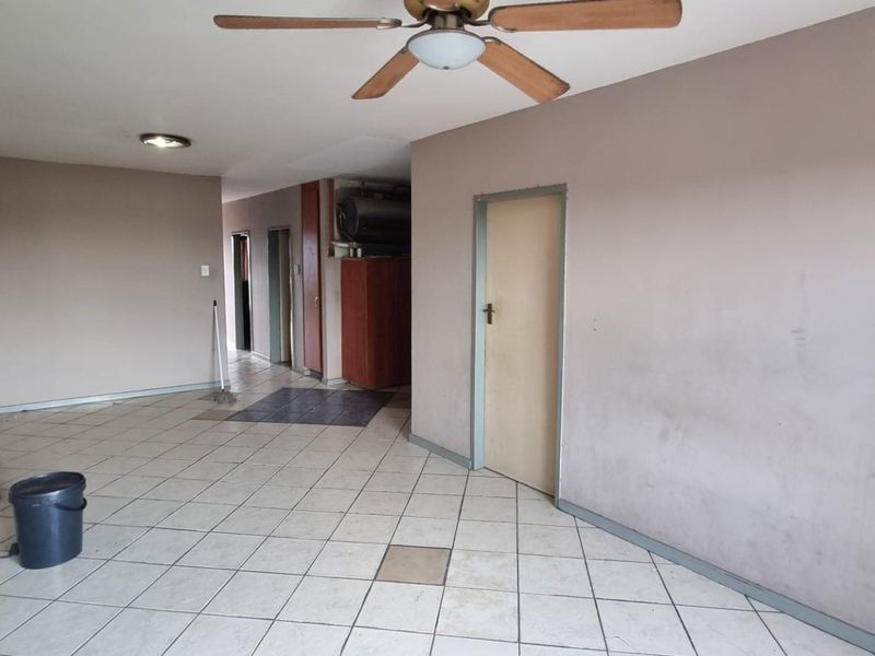 An empty living area featuring tiled flooring, a ceiling fan, and neutral wall tones, offering a blank canvas for renovation or interior design updates.
