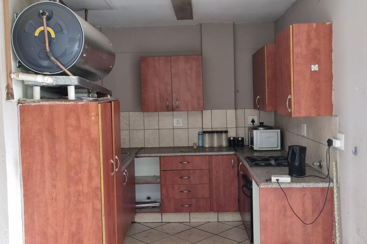 A compact kitchen featuring wood-look cabinetry, tiled backsplash, and an integrated electric hob, requiring some maintenance and cosmetic updates.