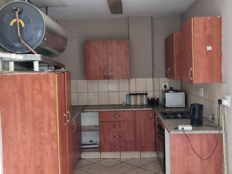 A compact kitchen featuring wood-look cabinetry, tiled backsplash, and an integrated electric hob, requiring some maintenance and cosmetic updates.
