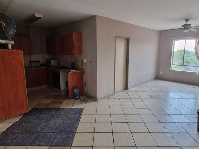 Open-plan living and kitchen area featuring tiled flooring, built-in cabinetry, and a ceiling fan, offering a blank canvas for renovation.