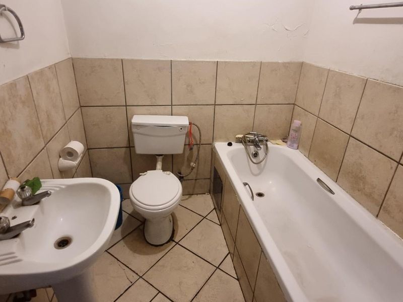 A functional bathroom featuring a pedestal basin, toilet, and bathtub with tiled walls and flooring, offering potential for modernization and cosmetic updates.