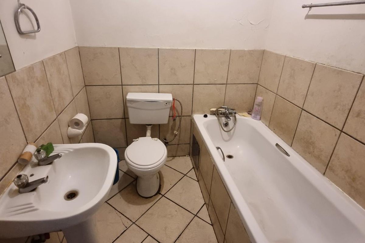 A functional bathroom featuring a pedestal basin, toilet, and bathtub with tiled walls and flooring, offering potential for modernization and cosmetic updates.