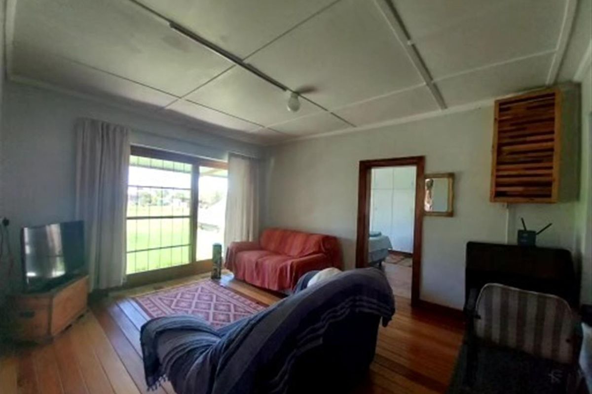 A living room featuring timber flooring, a sliding glass door providing outdoor access, and a ceiling with visible panel joints.