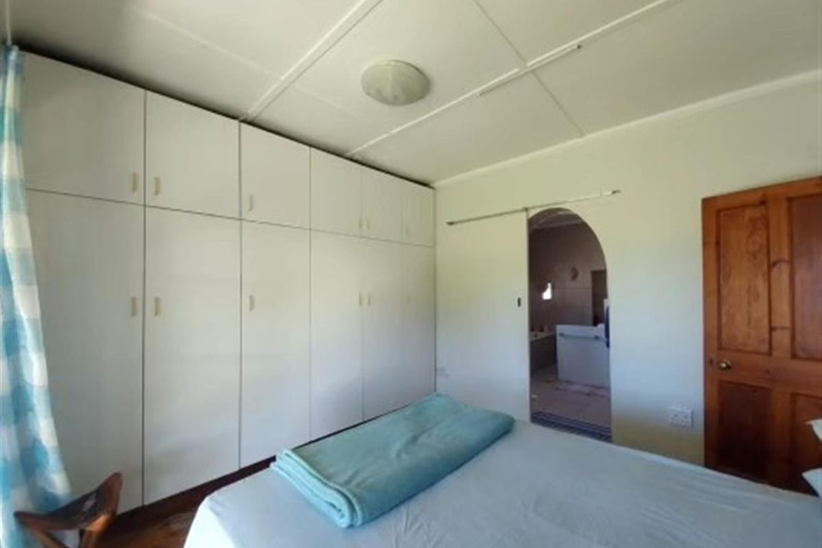 Bedroom featuring extensive built-in floor-to-ceiling cabinetry, wooden flooring, and an arched doorway leading to an adjoining bathroom.