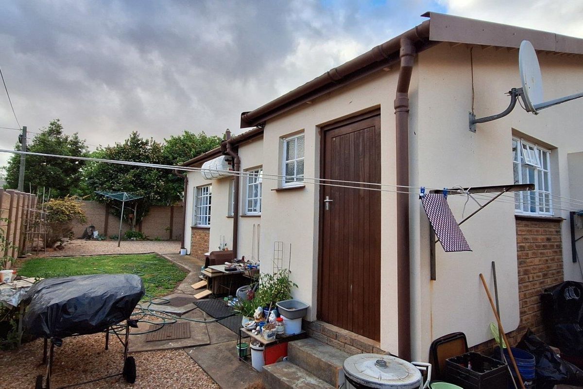 Rear view of the property showing the back facade, garden area, and exterior access door with paved pathway.