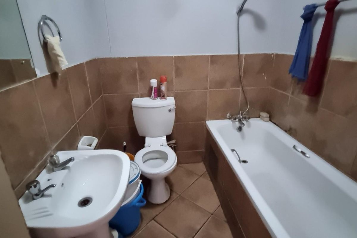 A functional bathroom featuring a pedestal washbasin, toilet, and a bathtub with a shower mixer, finished with brown wall and floor tiles.