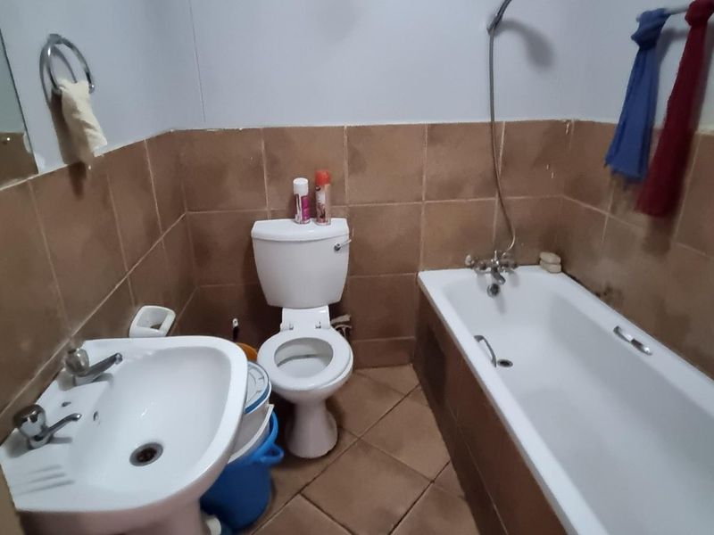 A functional bathroom featuring a pedestal washbasin, toilet, and a bathtub with a shower mixer, finished with brown wall and floor tiles.