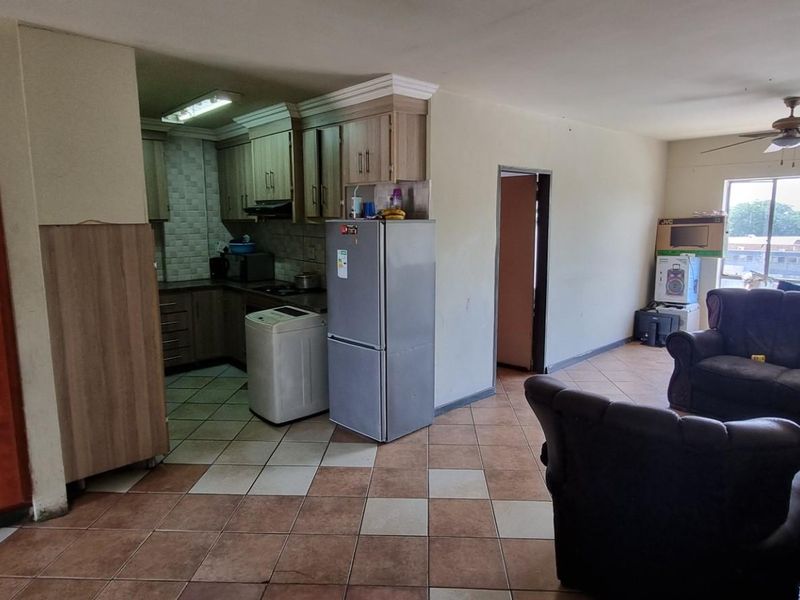 Open-plan living and kitchen area featuring tiled flooring, built-in cabinetry, and a ceiling fan, offering a functional layout in need of cosmetic updates.