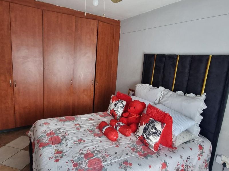 A bedroom featuring built-in wooden cupboards, tiled flooring, and a ceiling fan, offering a functional space with potential for cosmetic updates.