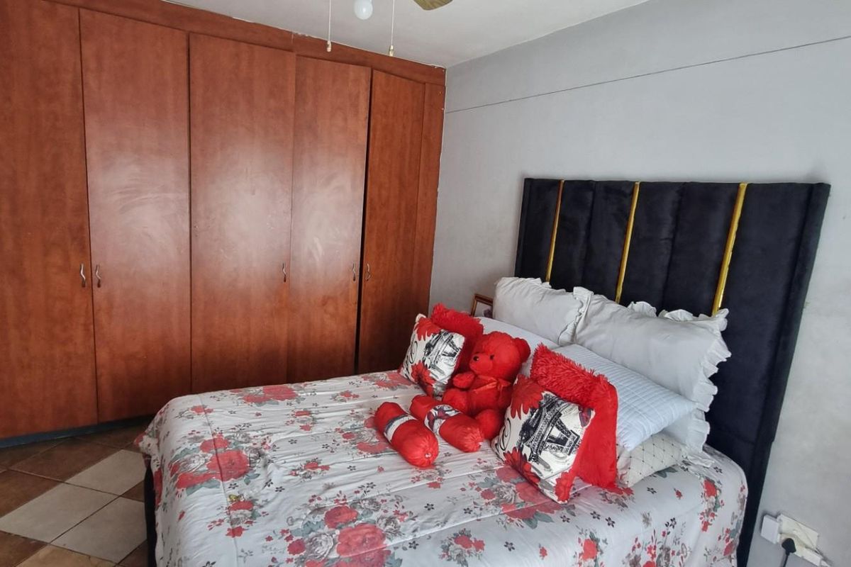 A bedroom featuring built-in wooden cupboards, tiled flooring, and a ceiling fan, offering a functional space with potential for cosmetic updates.