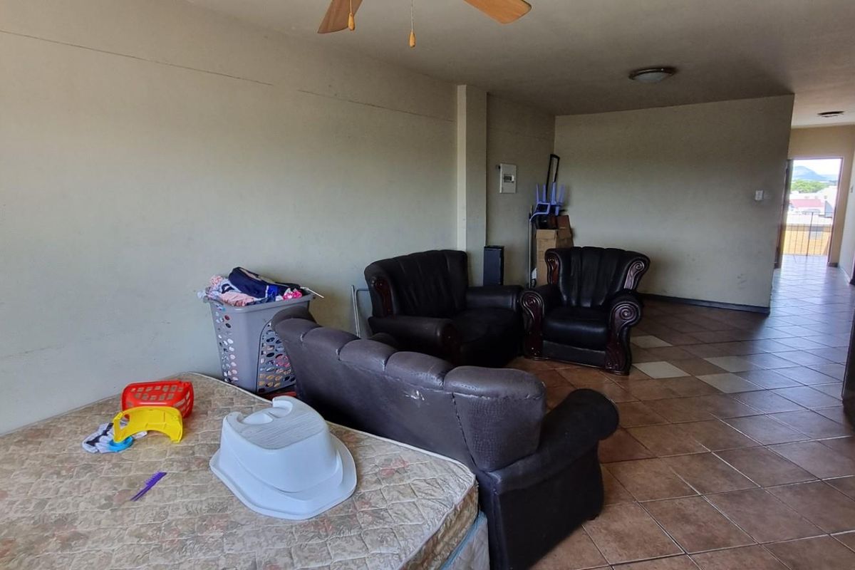 A spacious living area featuring ceramic floor tiles, a ceiling fan, and neutral wall finishes, offering a blank canvas for potential interior updates.