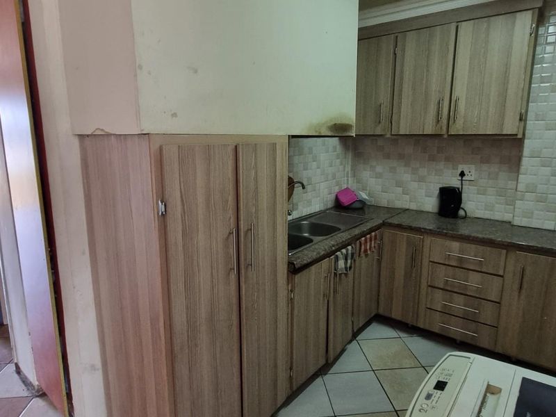Compact kitchen featuring laminate cabinetry, granite countertops, and a double basin sink, requiring minor cosmetic repairs to the wall finish.