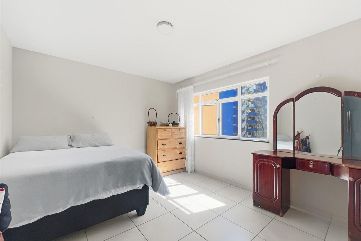 A bright bedroom featuring neutral wall tones, tiled flooring, and a large window allowing for natural light.