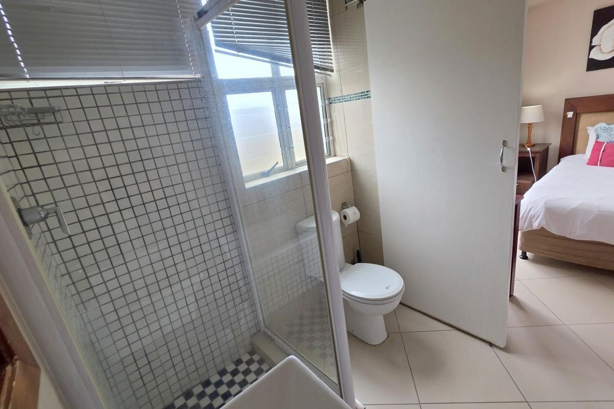 En-suite bathroom featuring a glass-enclosed shower with mosaic tiling, adjacent to a bedroom area with tiled flooring.