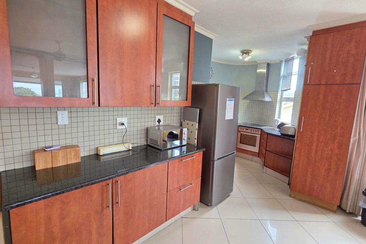 A functional kitchen featuring wood-tone cabinetry, dark granite countertops, a tiled backsplash, and a stainless steel extractor fan.