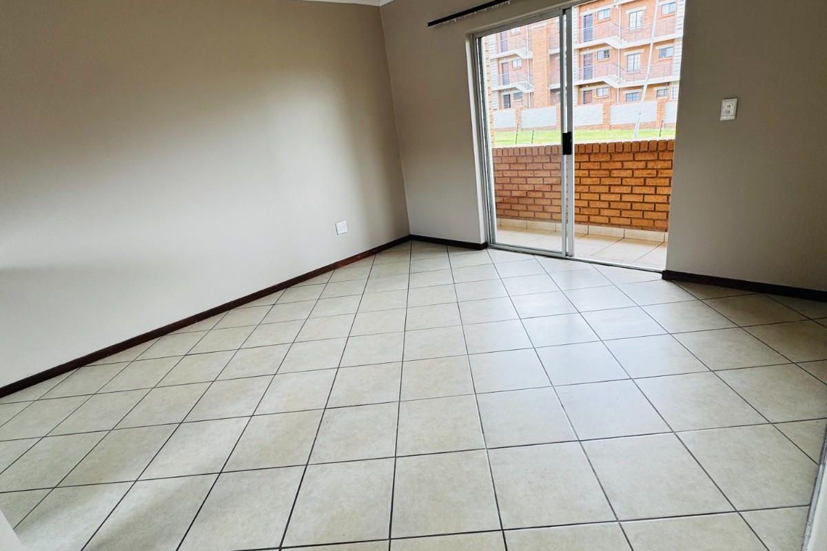 An empty living room featuring neutral wall paint, tiled flooring, and a sliding glass door providing access to a private balcony.