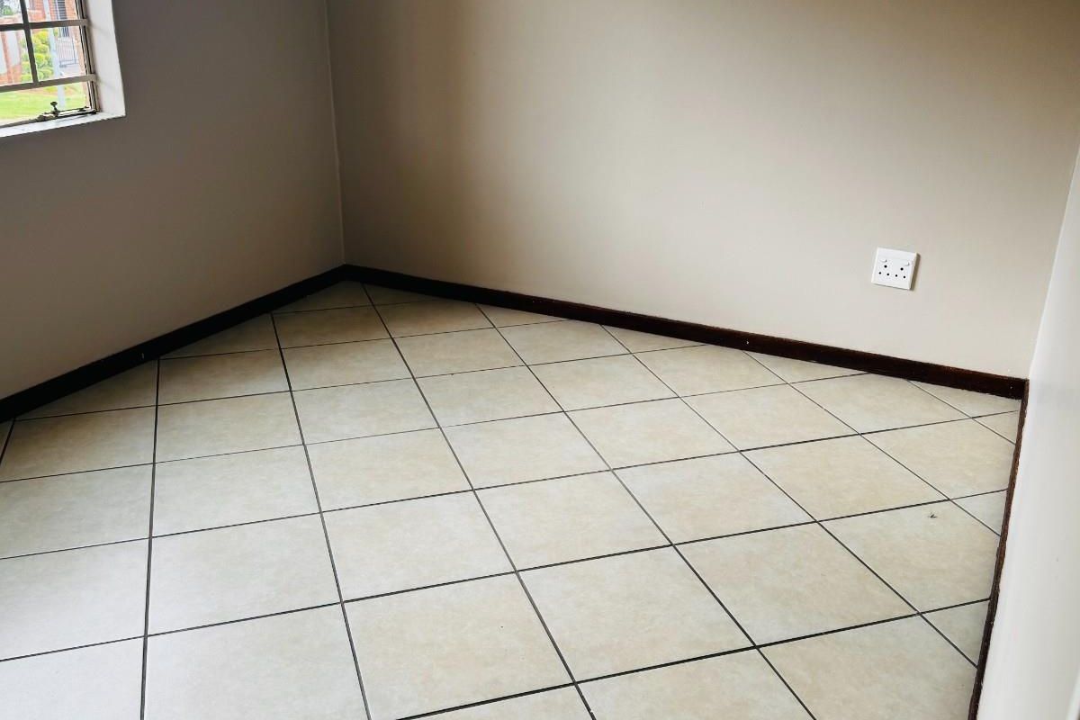 An empty bedroom featuring neutral wall paint, tiled flooring, and a window with security bars.