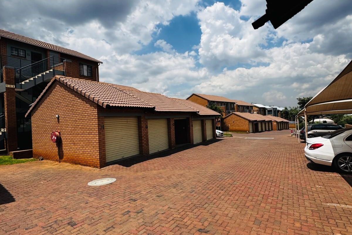 A view of the apartment complex parking area featuring multiple brick-built garages with tiled roofs and paved driveway access.