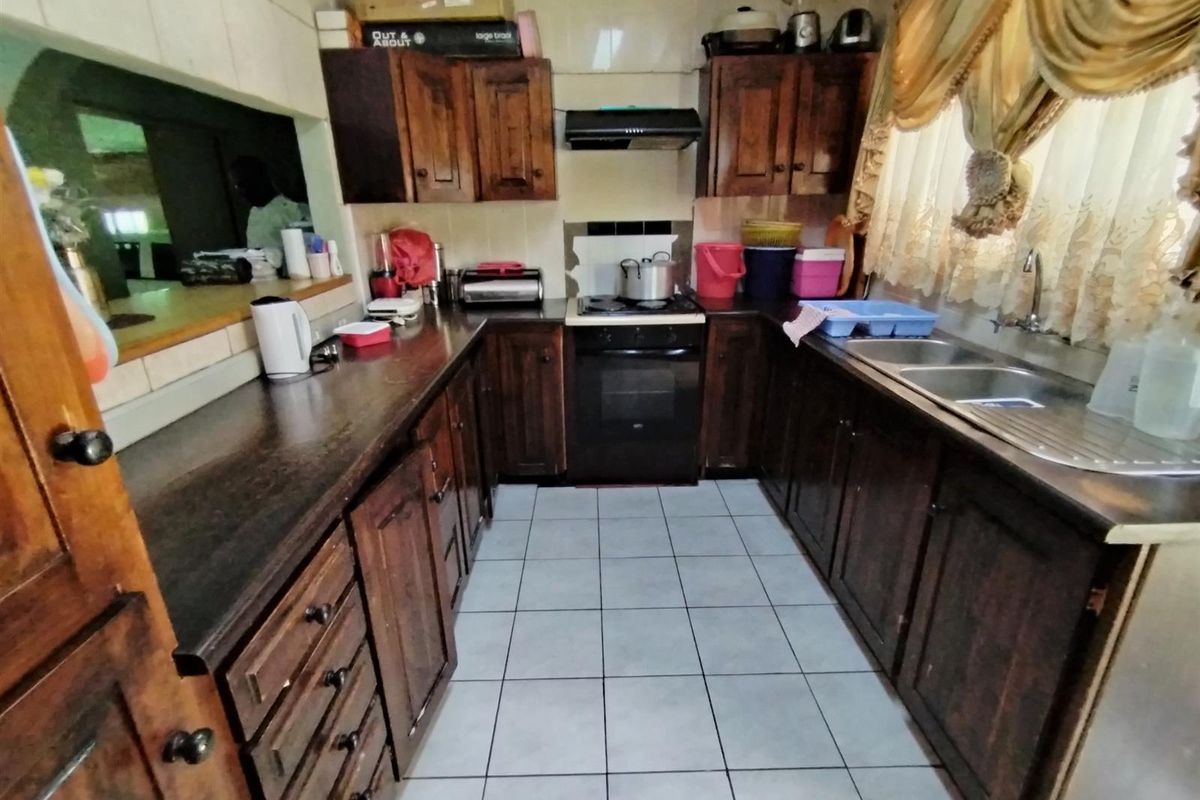 A functional U-shaped kitchen featuring dark wood cabinetry, a built-in oven and hob, extractor fan, and a double stainless steel sink.