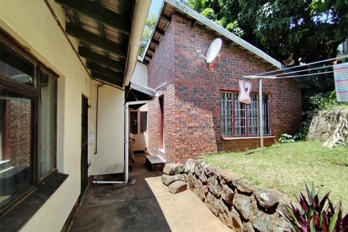 A view of the rear exterior of the house, featuring exposed brickwork, a concrete pathway, and a small terraced garden area.