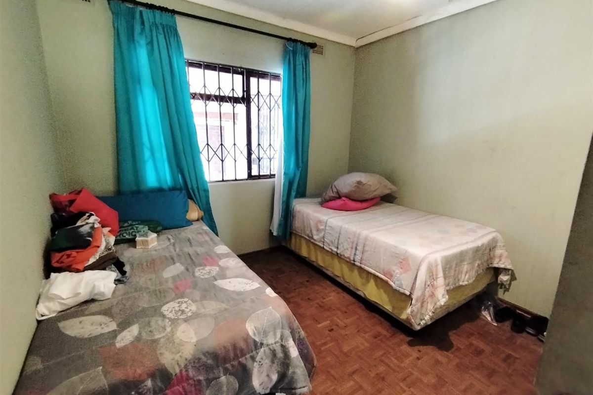A bedroom featuring parquet flooring, a security-barred window, and neutral wall finishes.