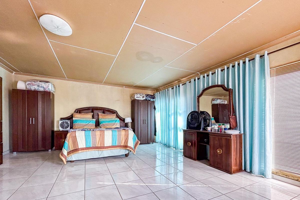 Spacious bedroom featuring tiled flooring, large windows with curtains, and built-in cabinetry, offering a functional layout with potential for cosmetic updates.