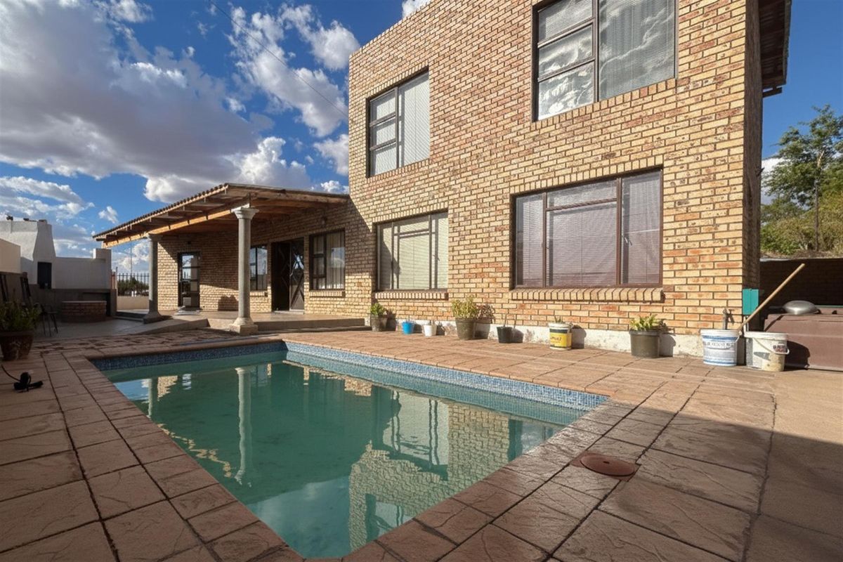 Rear exterior view featuring a swimming pool, paved patio area, and a two-story face-brick house with a covered veranda.