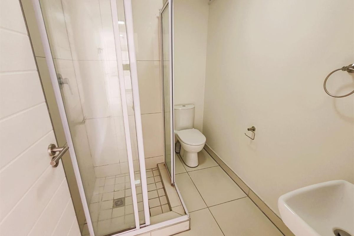 A functional bathroom featuring a glass-enclosed shower, a standard toilet, and a wall-mounted basin with neutral floor and wall tiling.
