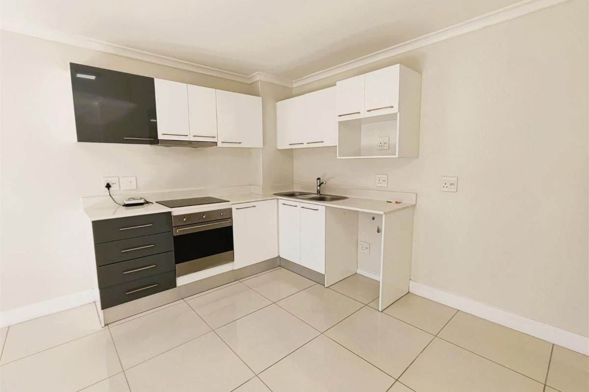 Modern kitchen featuring white and charcoal cabinetry, integrated oven, electric hob, extractor fan, and tiled flooring in an open-plan layout.