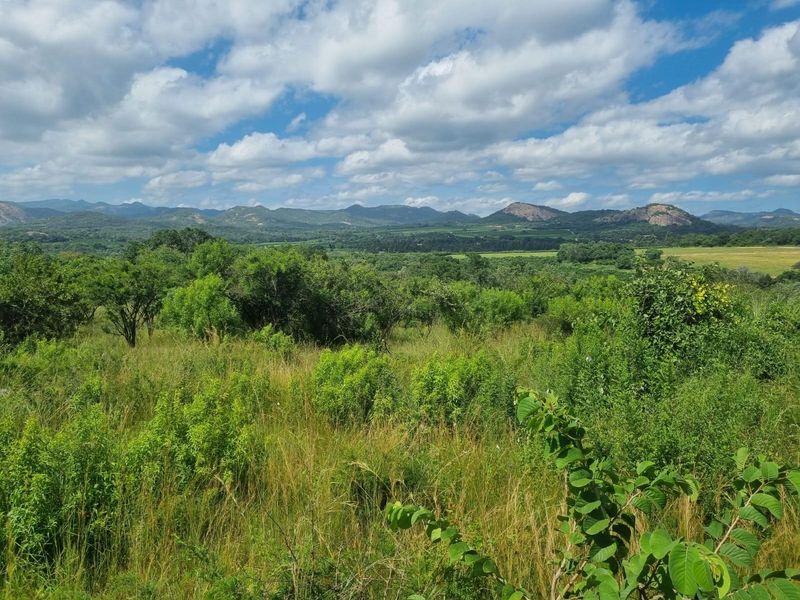 Expansive scenic view of the surrounding farm landscape, featuring lush green vegetation and distant mountain ranges under a clear blue sky.