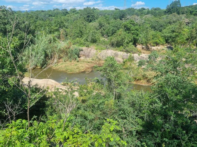 A scenic view of a natural river flowing through a lush, green landscape with prominent rock formations and dense surrounding forest.