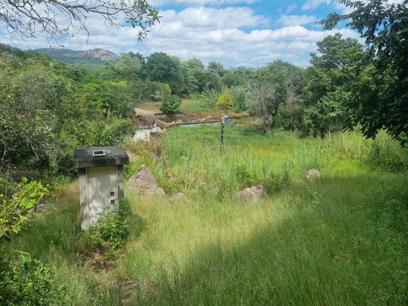 A scenic view of the farm landscape featuring natural vegetation, a small utility structure, and a weir in the distance.