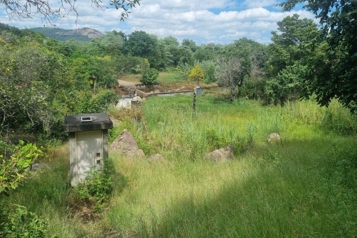 A scenic view of the farm landscape featuring natural vegetation, a small utility structure, and a weir in the distance.