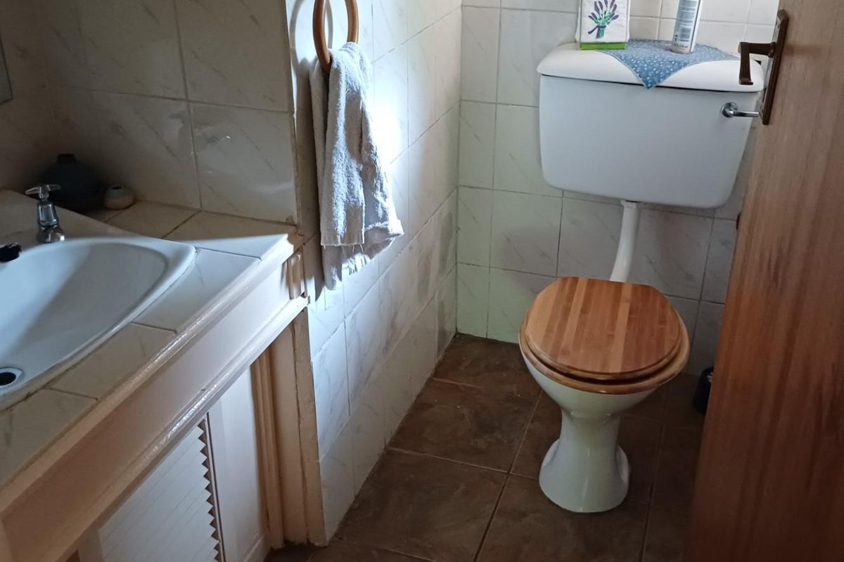 A compact bathroom featuring a tiled vanity with integrated basin, a standard toilet, and tiled flooring.