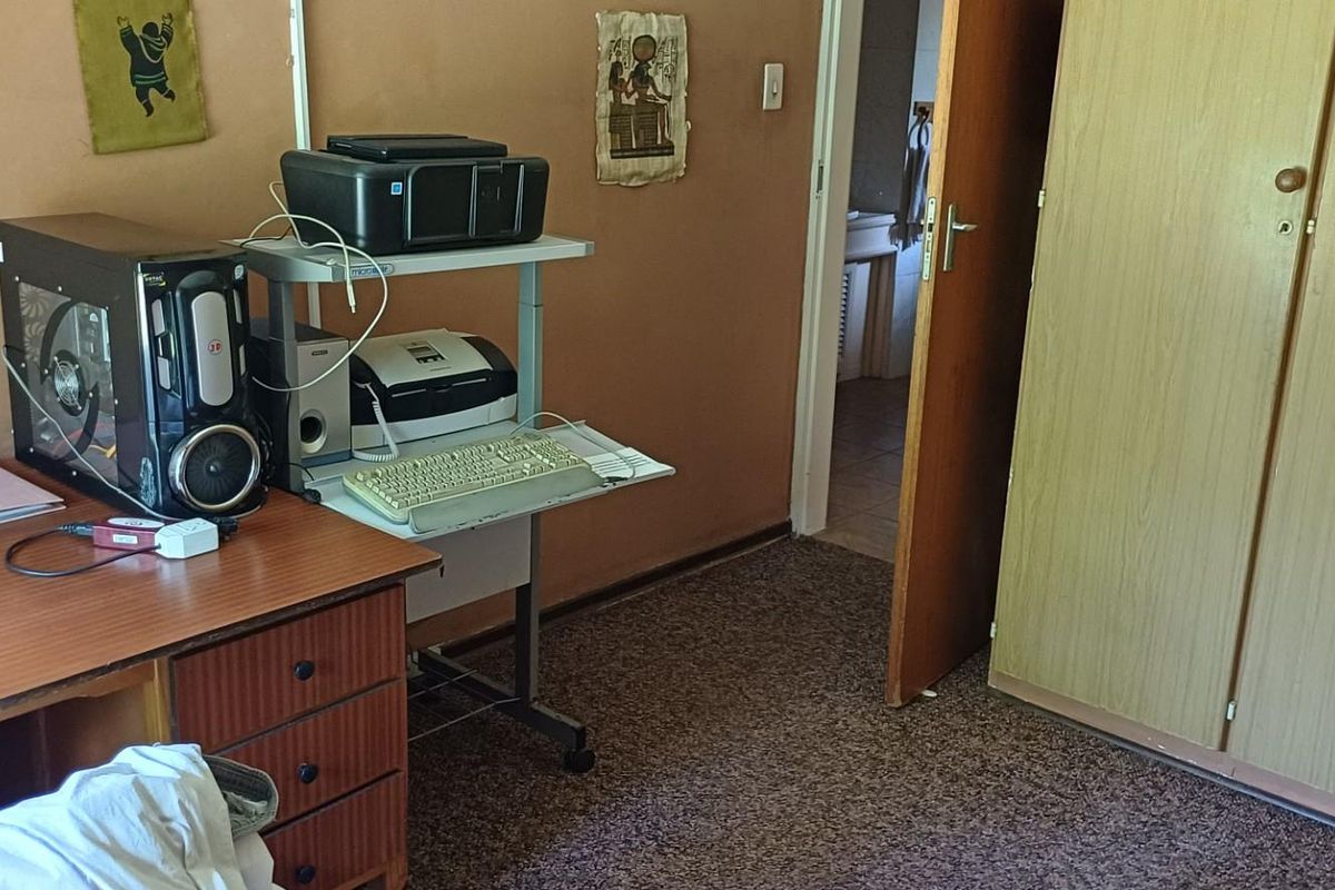 A bedroom featuring built-in wooden cupboards and carpeted flooring, with an adjacent doorway leading to a bathroom area.