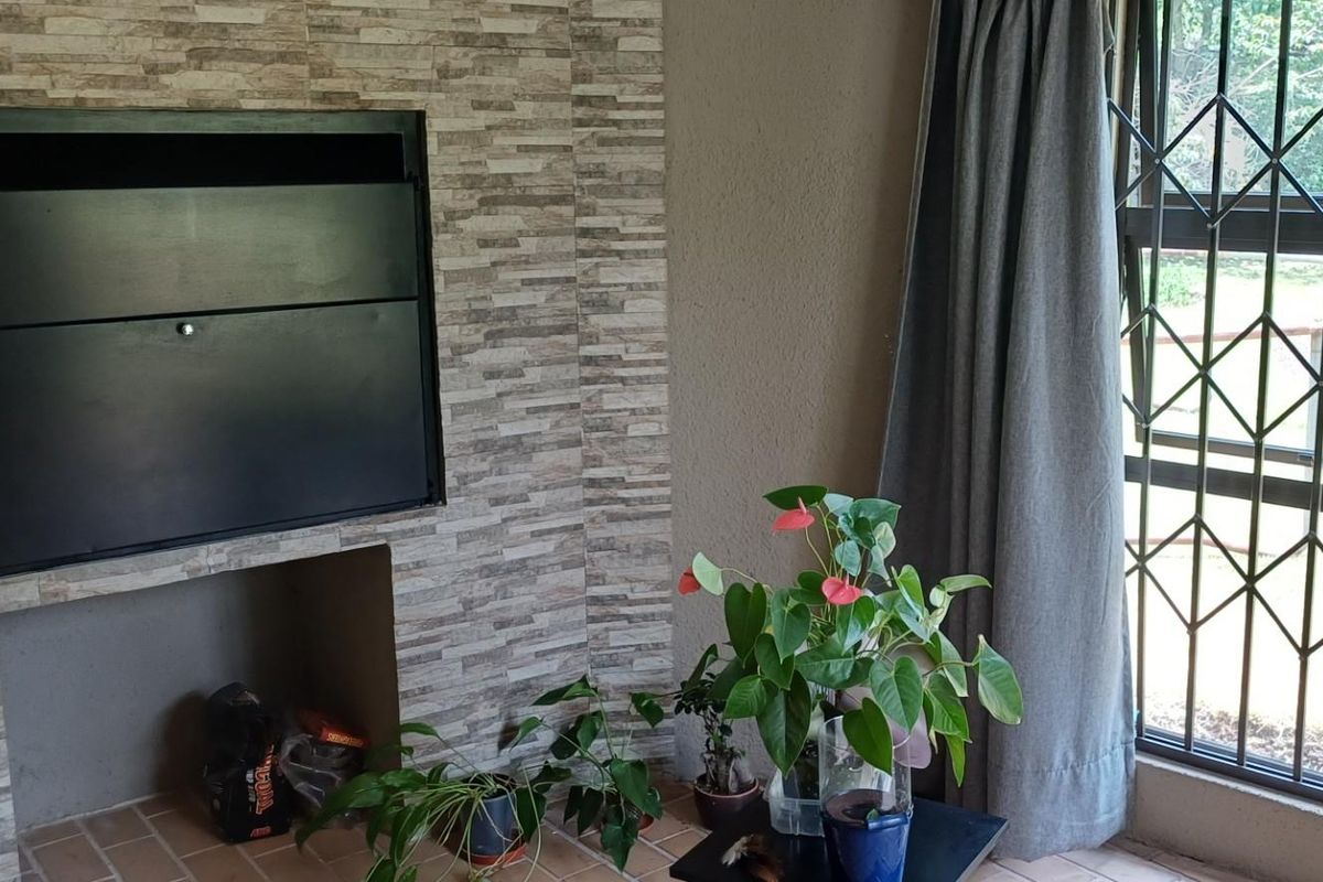 A living room area featuring a built-in fireplace with stone-cladding surround and a window fitted with security bars.